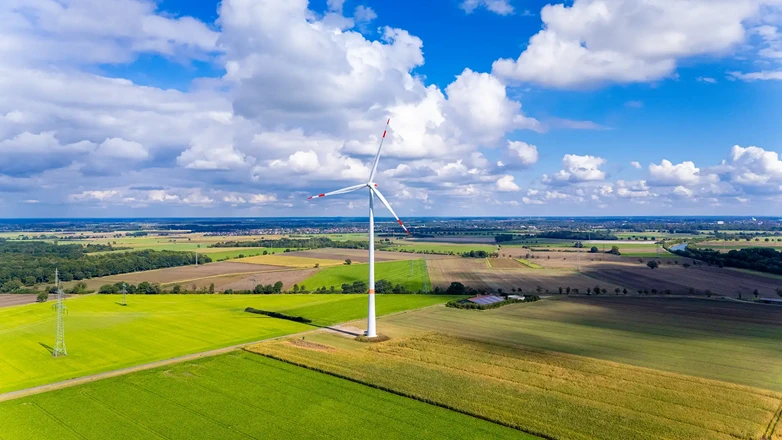 Windkraftanlage mit Turm, Gondel und Rotor vor Feldern und Waldflächen